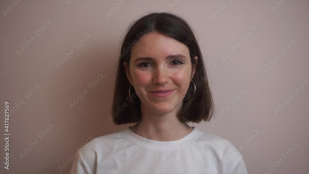 Confident smiling young european woman looking at camera. Happy millennial casual professional lady with white teeth pretty face posing for close up portrait indoors. Slow motion. Confident smiling young european woman looking at camera. Happy millennial casual professional lady with white teeth pretty face posing for close up portrait indoors. Slow motion.