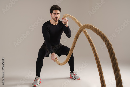 Handsome athletic sportsman working out with battle ropes
