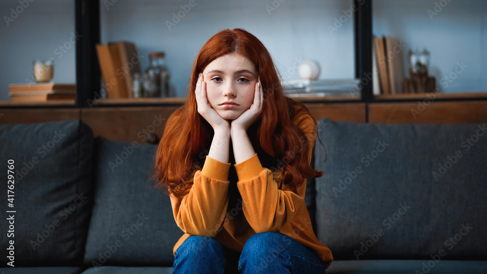 Red haired teenager looking at camera while sitting on couch at home Red haired teenager looking at camera while sitting on couch at home