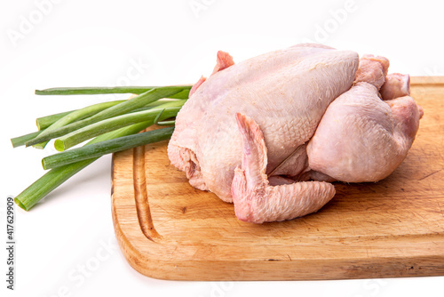 Raw chicken and a bunch of green onions on a cutting board. Isolate on white background 