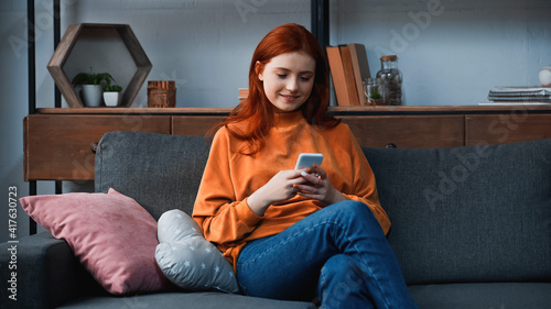 Foto Positive teenager using smartphone in living room