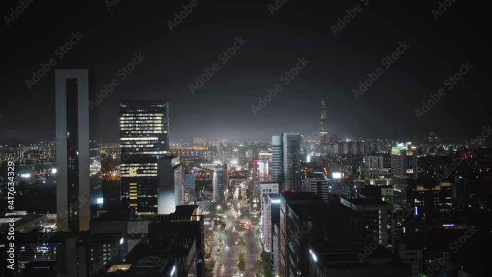 Camera moving up high between modern skyscrapers showing beautiful panorama of Seoul Gangnam District on the night, and then getting lower and flying above busy road street with a lot of traffic.