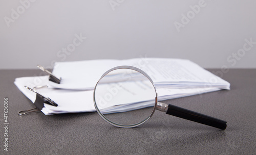 Stack of paper documents with magnifying glass, on table.