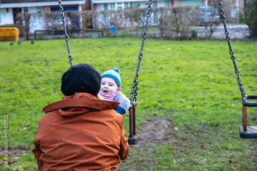 Mom swinging her baby boy in swing outdoor. Mother and her child having fun together outdoor. Happy family concept