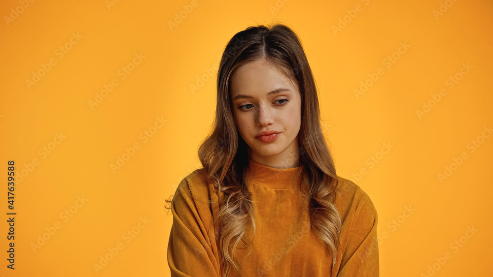 pensive teenage girl in sweater looking down isolated on yellow