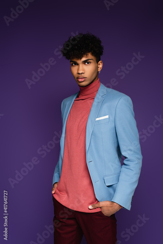 african american man in blue blazer standing with hands in pockets on purple