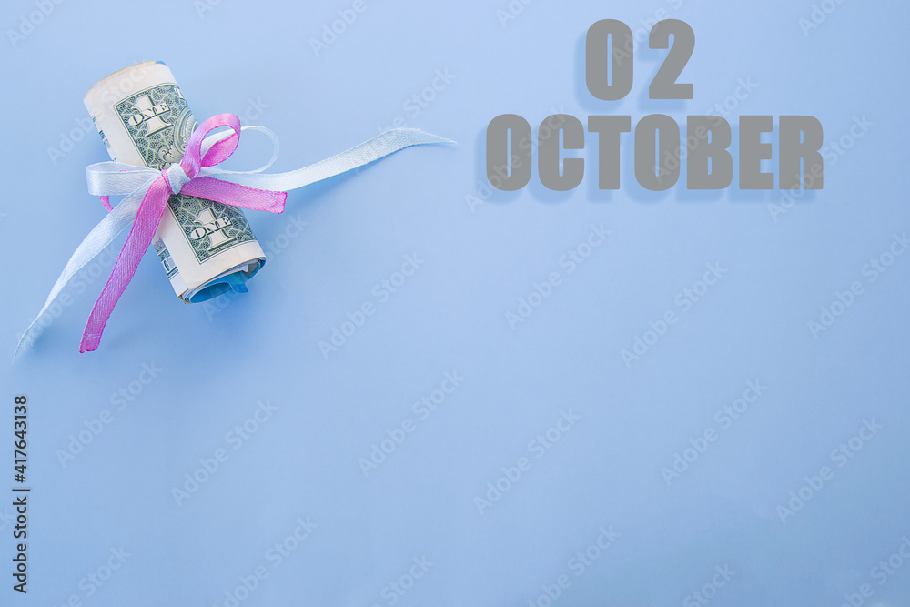 calendar date on blue background with rolled up dollar bills pinned by blue and pink ribbon with copy space. October 2 is the second day of the month