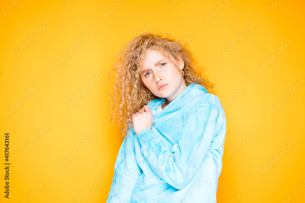 Beautiful woman in a blue sweater with curly hair stands on an orange background Beautiful woman in a blue sweater with curly hair stands on an orange background