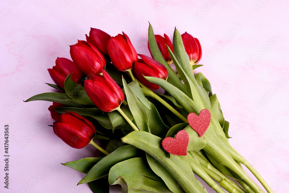 Red tulips bouquet and red hearts on a pink background. Valentine's Day, Woman's Day and Mother's Day concept. View from the top Red tulips bouquet and red hearts on a pink background. Valentine's Day, Woman's Day and Mother's Day concept. View from the top