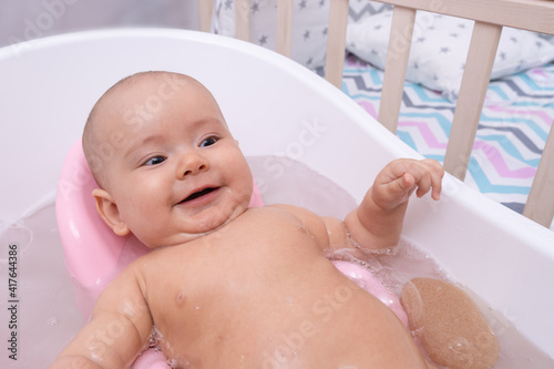 The baby lies in the bathroom and laughs. Bathing a newborn