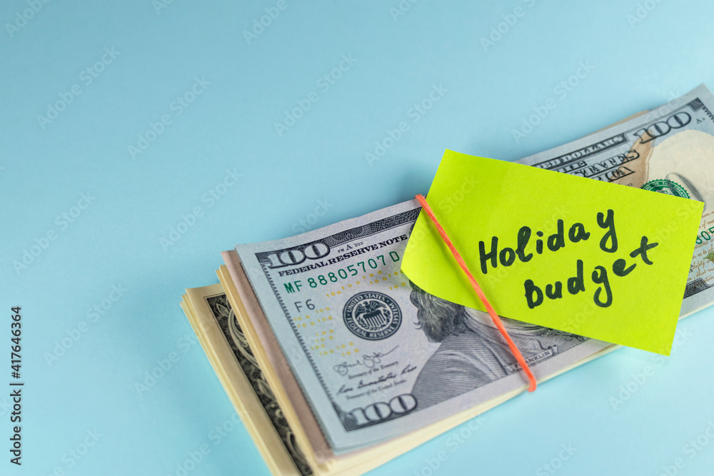 Text written note Holiday budget, dollars cash money in rubber band with note, on copy space background - concept of financial planning of set budget for Christmas or holiday Text written note Holiday budget, dollars cash money in rubber band with note, on copy space background - concept of financial planning of set budget for Christmas or holiday