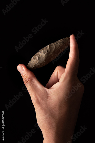 A hand holds a perfectly preserved paleolithic javelin point on a black background photo