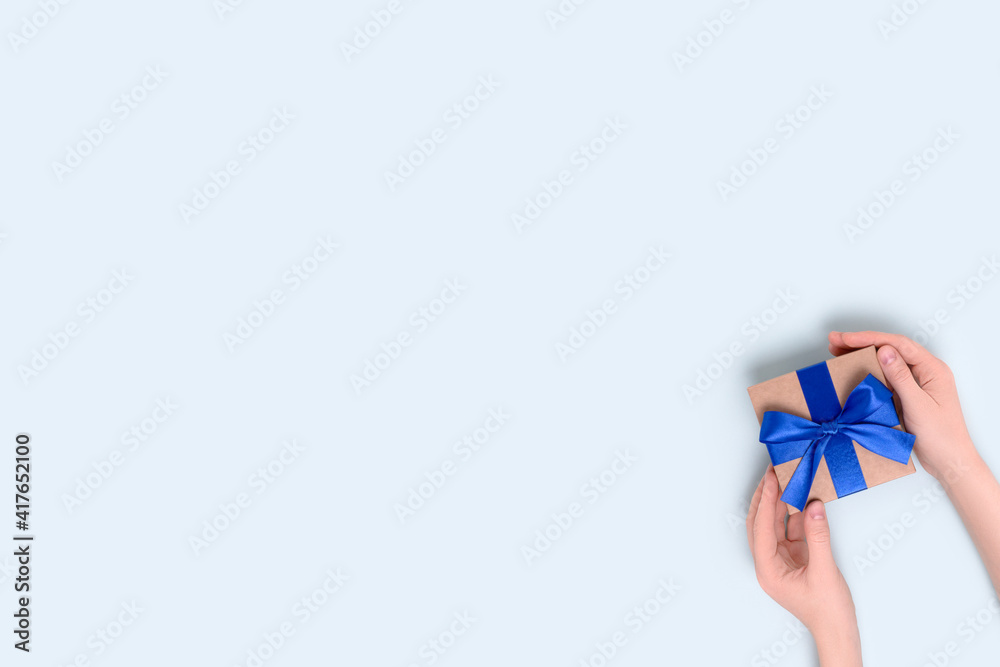 Female hands hold wrapped gift box on a blue pastel background. Present tied with a ribbon. Female hands hold wrapped gift box on a blue pastel background. Present tied with a ribbon.