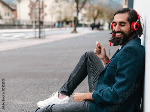 hombre feliz y motivado sentado en el suelo contra una pared blanca en la calle escuchando música   photo