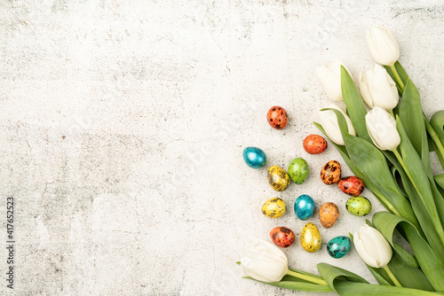 Top view of white tulips and colored easter eggs on concrete backgrund with copy space