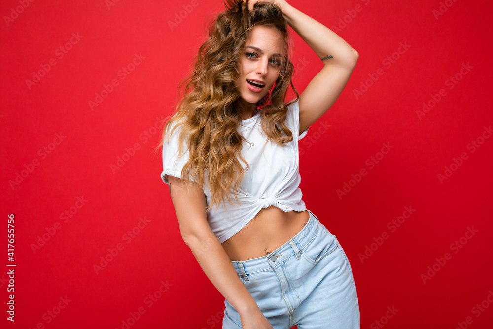 Young beautiful curly blonde woman with sexy expression, cheerful and happy face wearing casual white t-shirt isolated over red background with copy space Young beautiful curly blonde woman with sexy expression, cheerful and happy face wearing casual white t-shirt isolated over red background with copy space