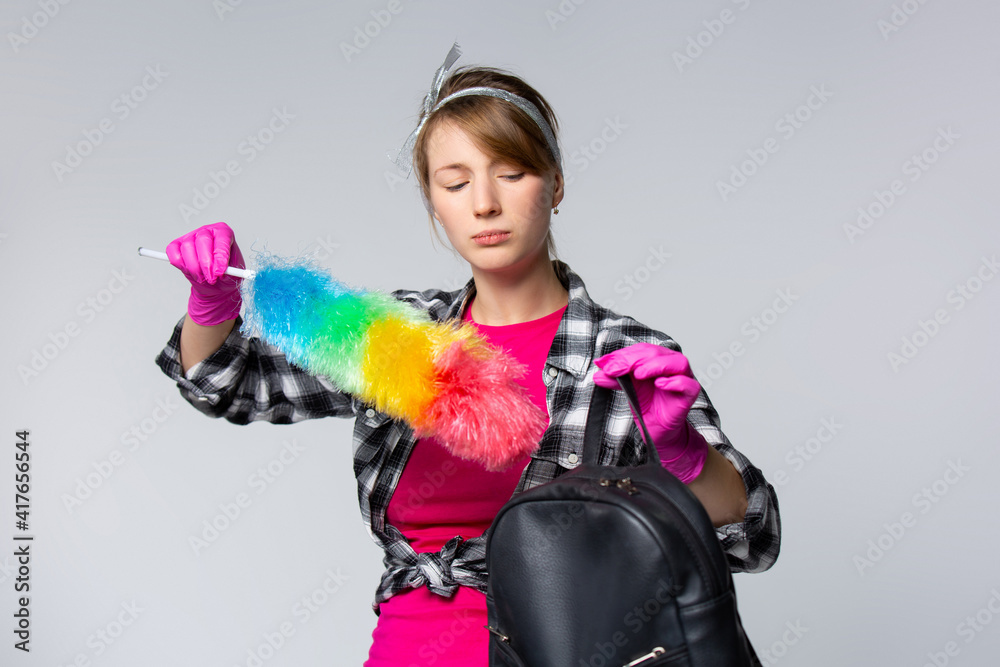 Concentrated young caucasian cleaning woman with pink rubber gloves cleaning her backpack. Concentrated young caucasian cleaning woman with pink rubber gloves cleaning her backpack.