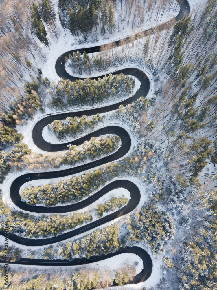 Winding road aerial view by drone. Brasov, Romania. There are huge snow mountains and long winding road in this area. This is a great place to drive and stop during a road trip.