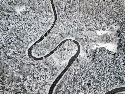 Winding road aerial view by drone. Brasov, Romania. There are huge snow mountains and long winding road in this area. This is a great place to drive and stop during a road trip. © Rafaila Gheorghita