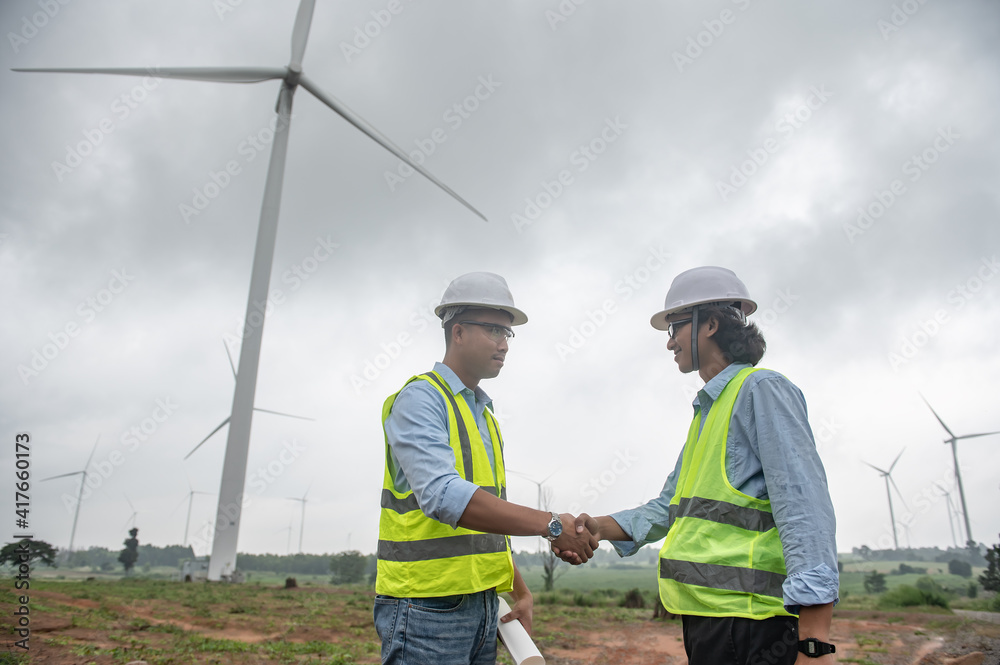 Two engineers working and holding the report at wind turbine farm Power Generator Station on mountain,Thailand people Two engineers working and holding the report at wind turbine farm Power Generator Station on mountain,Thailand people