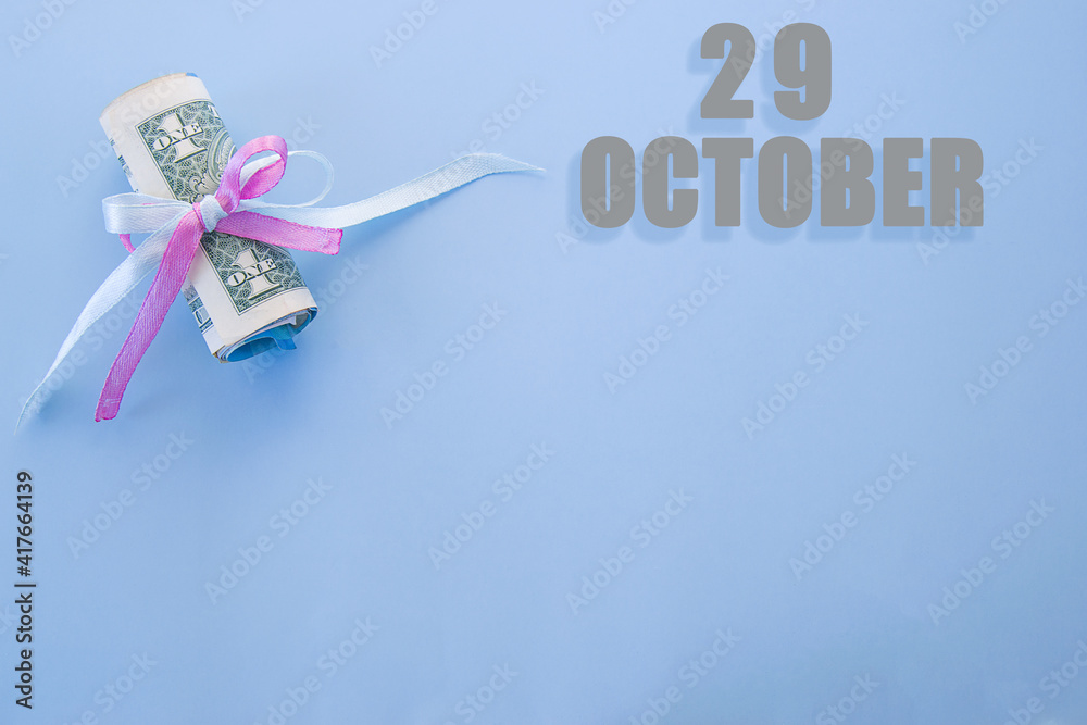 calendar date on blue background with rolled up dollar bills pinned by blue and pink ribbon with copy space. October 29 is the twenty-ninth day of the month