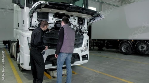 Professional male mechanic in a repair service stands with the car owner near an open truck after repairs. men discuss breakdowns decide to repair transport. Modern truck repair service