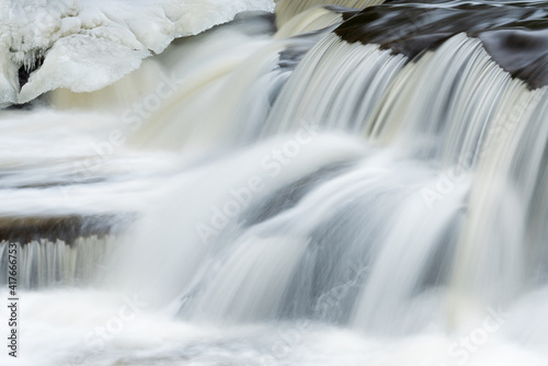 Winter landscape of a cascade at Bond Falls captured with motion blur and framed by ice and snow  Michigan s Upper Peninsula  USA