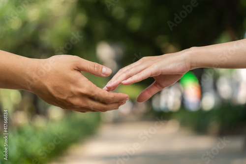 Concept of human relation, community, togetherness, teamwork, love, symbolism, culture and history. Hand of male and female reaching to each other. Nature background. Selective focus. © CravenA