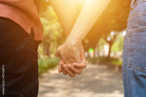 Couple hold hands in the autumn or summer park on sunset. Closeup of loving couple holding hands while walking.