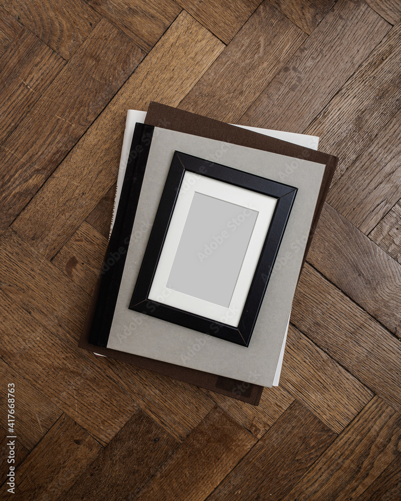 Still life scene. Books and empty picture frame mockup on wooden desk, table. Elegant working space, home office concept. Scandinavian interior design. Room in sunlight.