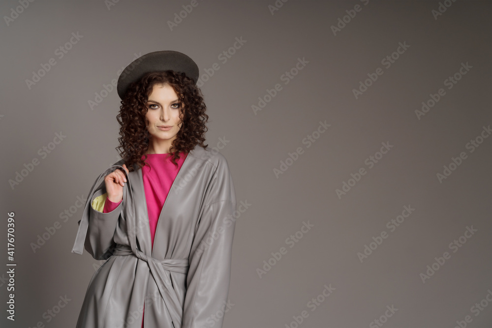 Fototapeta premium Studio shot of curly fashion model in bright pink clothes and leather jacket on gray background with copy space