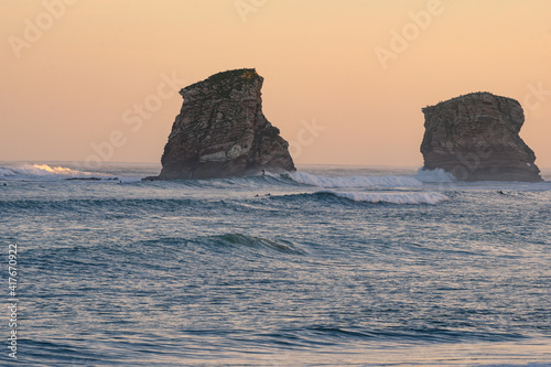 the twins, rocks of henday beach at dawn surrounded by waves and in the distance people surfing