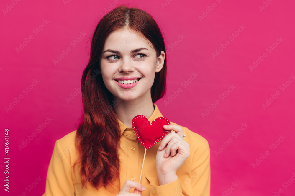 emotional woman with heart on a stick and yellow shirt on a pink background