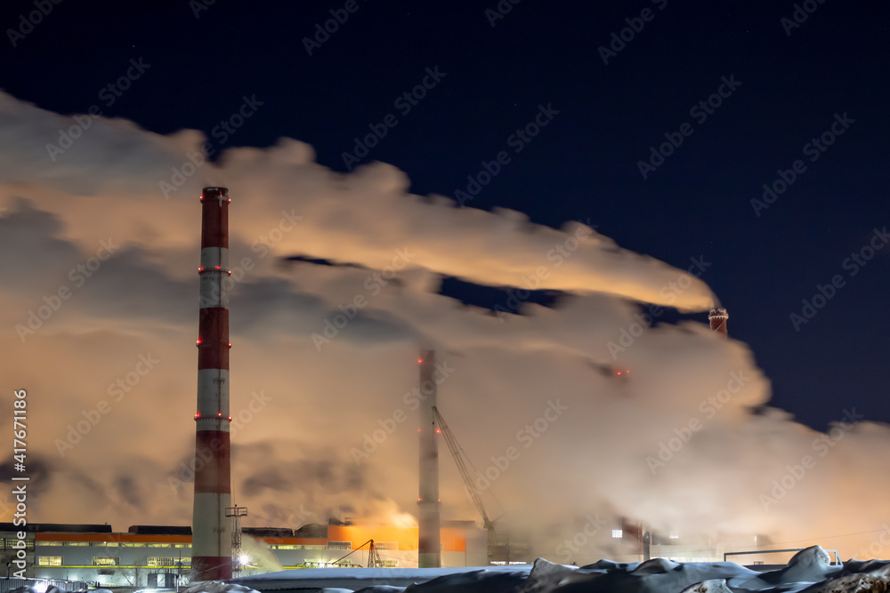 Tall chimneys of a large factory against the backdrop of the night sky.