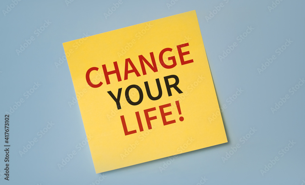Yellow reminder sticky note on a blue wall with CHANGE YOUR LIFE text. Motivation concept.