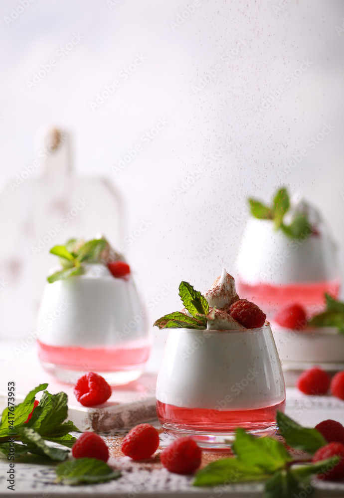 Creamy dessert with raspberry jelly in a clear glass, with mint, berries and cocoa sprinkles on a white wooden table on a light background. Background image, copy space, vertical, rustic