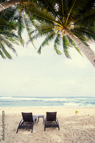 Tropical landscape. Sunloungers on sand beach with coconut palm trees.