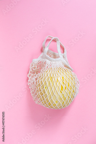 Ripe honeydew melon in eco-friendly cotton mesh on pink background close up. Copy space.Top view.