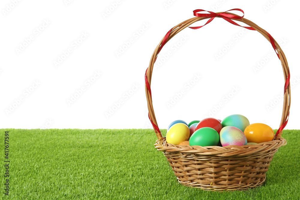 Wicker basket with Easter eggs on green grass against white background. Space for text Wicker basket with Easter eggs on green grass against white background. Space for text