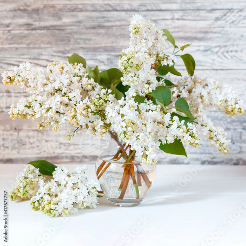 White lilac bouquet in glass vase on wooden table. Spring branches of blooming lilac festive bouquet of flowers.