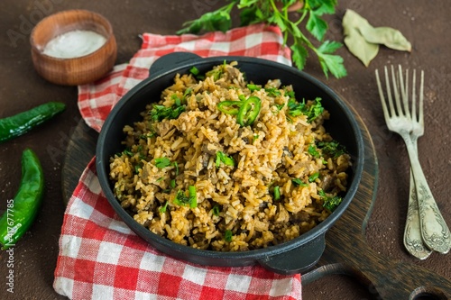 Dirty rice, Cajun cuisine dish, rice with liver, minced pork, aubergine , green pepper and spices in a cast iron skillet on a brown concrete background.