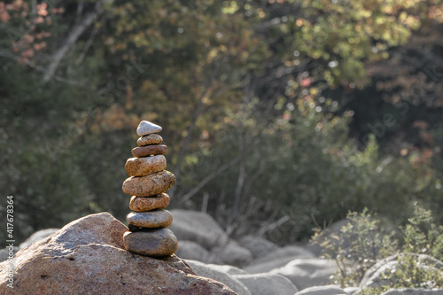 Zen stones balanced on top of bigger rock with foliage behind