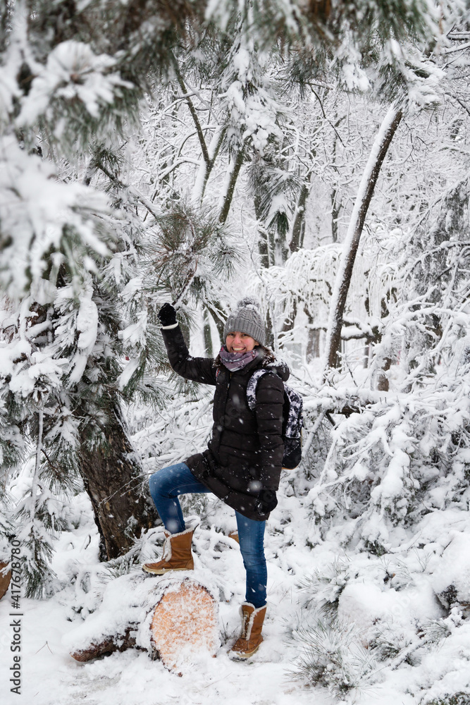 Smiling young woman standing on fallen tree after sleet load and snow in a snow-covered winter park. Girl enjoying snowy winter, frosty day. Walk in winter forest