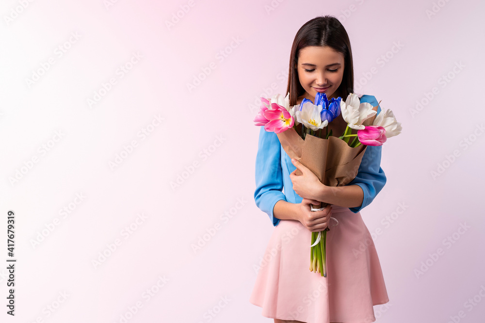 Studio shot of good looking woman smells tulip flowers, enjoys pleasant odor, stylish clothes indoor. Lovely caucasian lady hold beautiful bouquet of spring flowers. Neon pink background Studio shot of good looking woman smells tulip flowers, enjoys pleasant odor, stylish clothes indoor. Lovely caucasian lady hold beautiful bouquet of spring flowers. Neon pink background