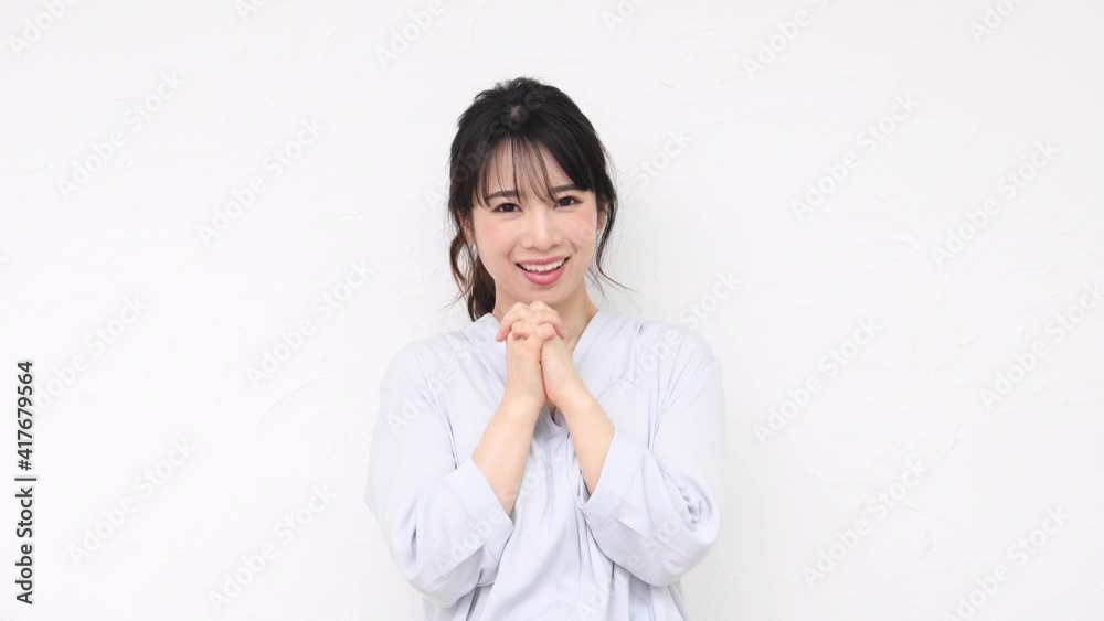 白い壁の前に立ってお願いのジェスチャーをする若い女性 白い壁の前に立ってお願いのジェスチャーをする若い女性