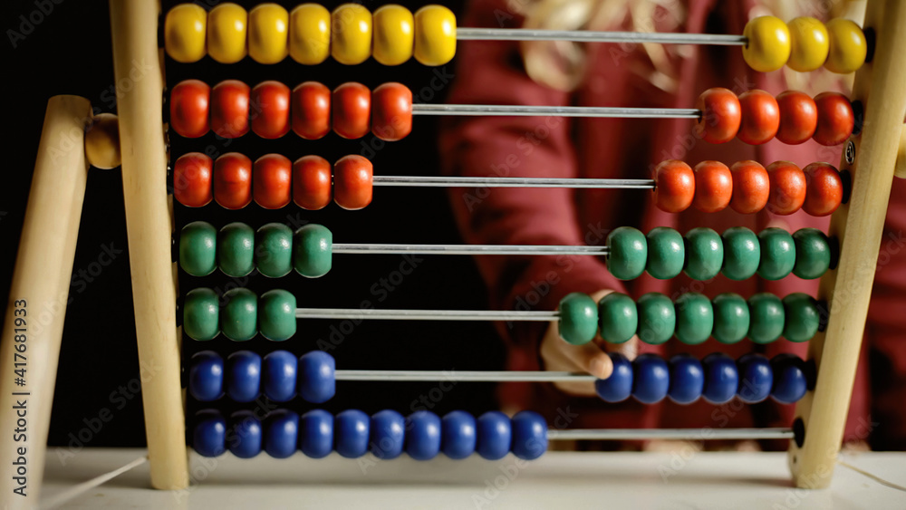 A little girl playing with an abacus, learning to count. Front view, detail of the beads and of the hand shifting them.
A little girl playing with an abacus, learning to count. Front view, detail of the beads and of the hand shifting them.