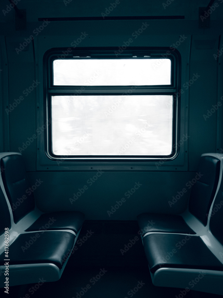 Fototapeta premium Dark empty cabin of a passenger train car with seats and a window in the center behind which is a white sky.