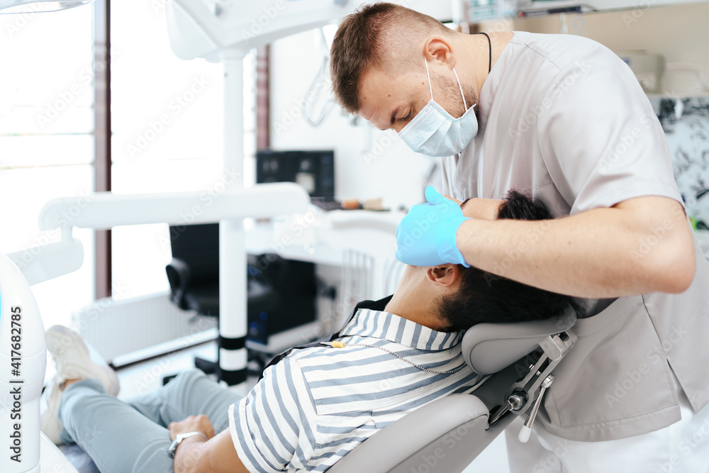 Smiling young man sitting in dentist chair while doctor examining his teeth Smiling young man sitting in dentist chair while doctor examining his teeth