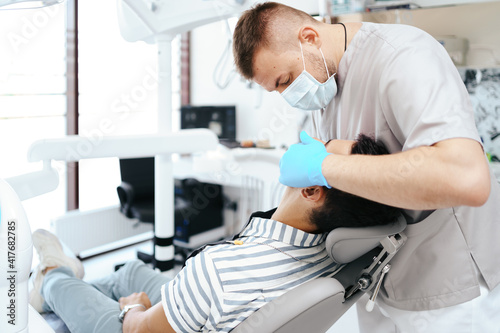 Smiling young man sitting in dentist chair while doctor examining his teeth