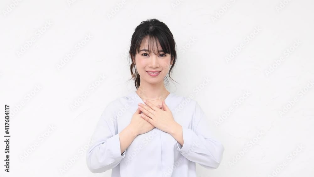 白い壁の前に立って胸に手を当てる若い女性 白い壁の前に立って胸に手を当てる若い女性